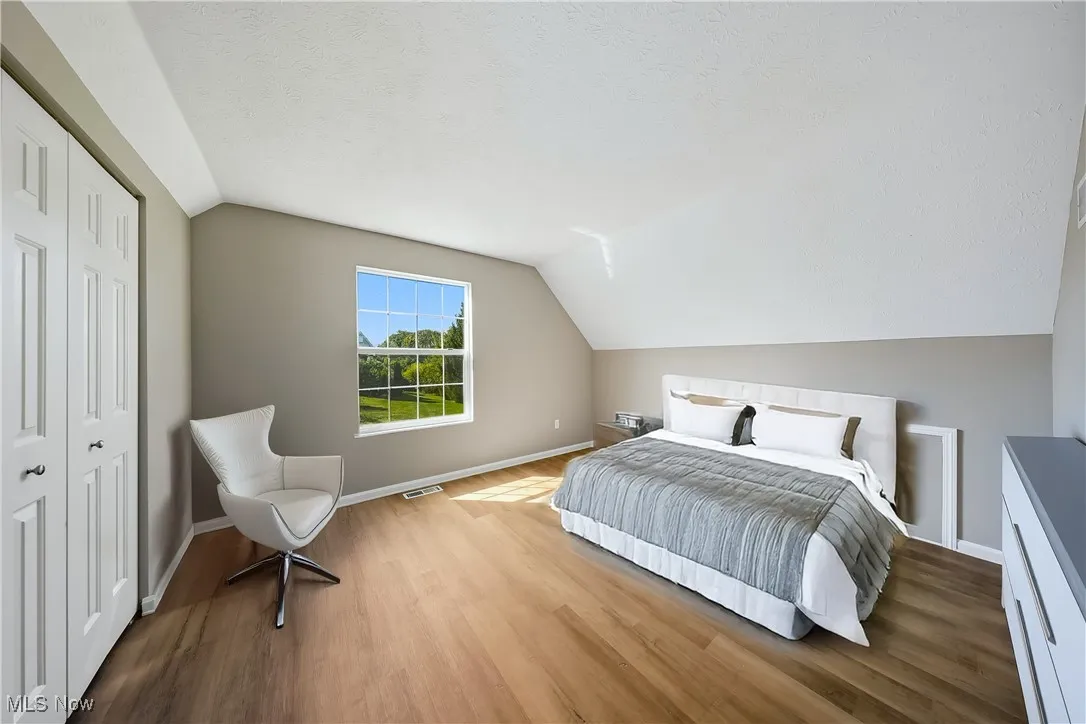 virtually staged Bedroom featuring lofted ceiling, a closet, wood finished floors, and a textured ceiling