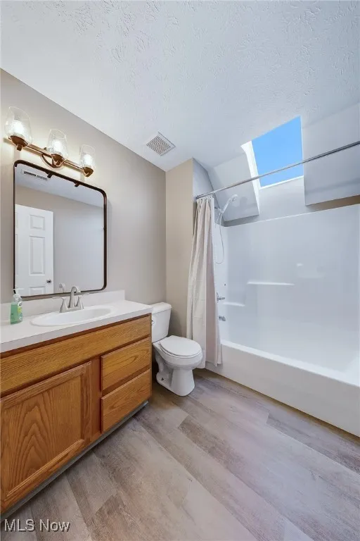Bathroom with shower / tub combo with curtain, vanity, light wood-style flooring, a skylight, and a textured ceiling