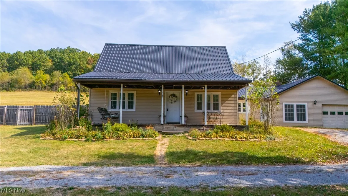 View of front facade featuring a porch, a metal roof, driveway, a garage, and an outdoor structure