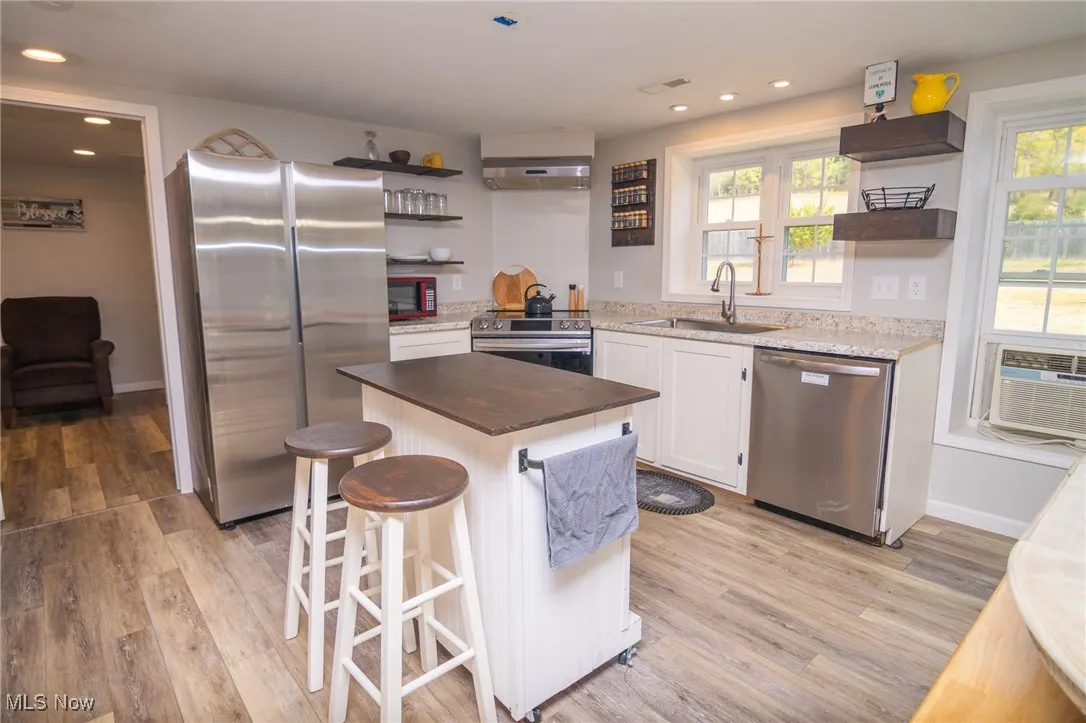 Kitchen featuring open shelves, stainless steel appliances, a kitchen bar, wood counters, and a center island