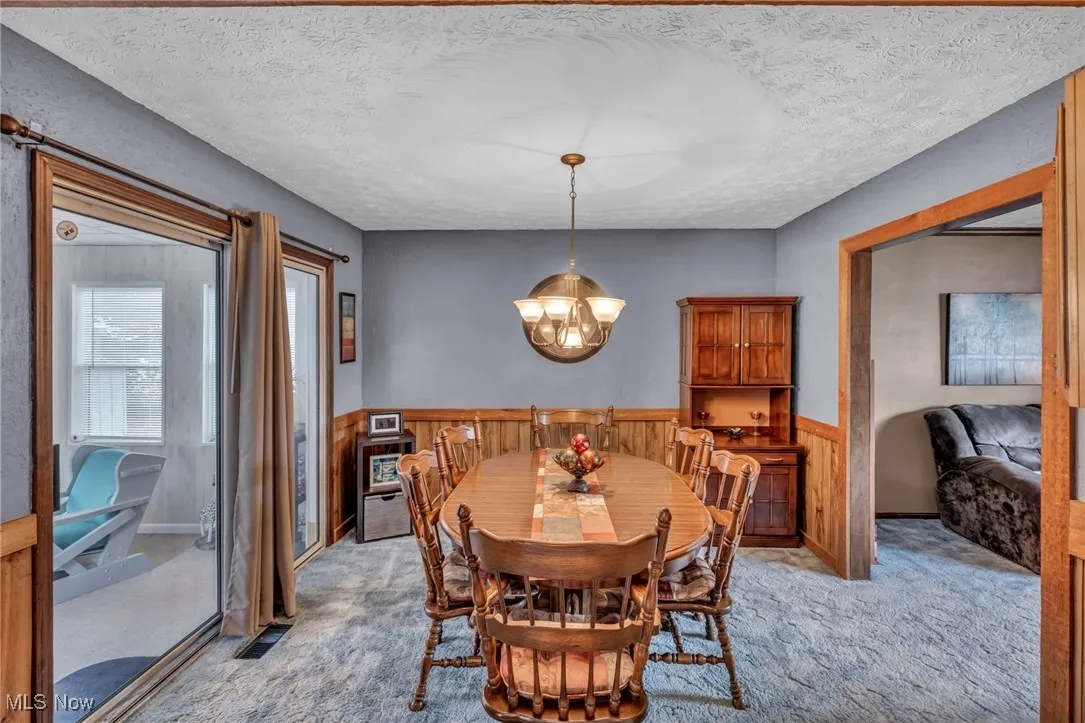 Carpeted dining area featuring a textured ceiling, wooden walls, a wainscoted wall, and a chandelier