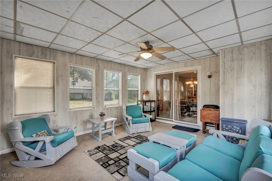 Sunroom featuring a ceiling fan, carpet, a patio area, a drop ceiling, and wooden walls