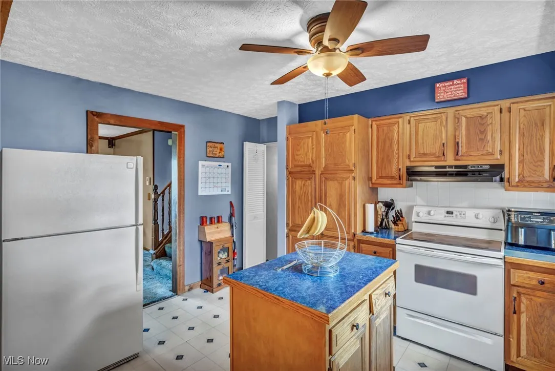 Kitchen with freestanding refrigerator, white electric range oven, a textured ceiling, decorative backsplash, and ceiling fan