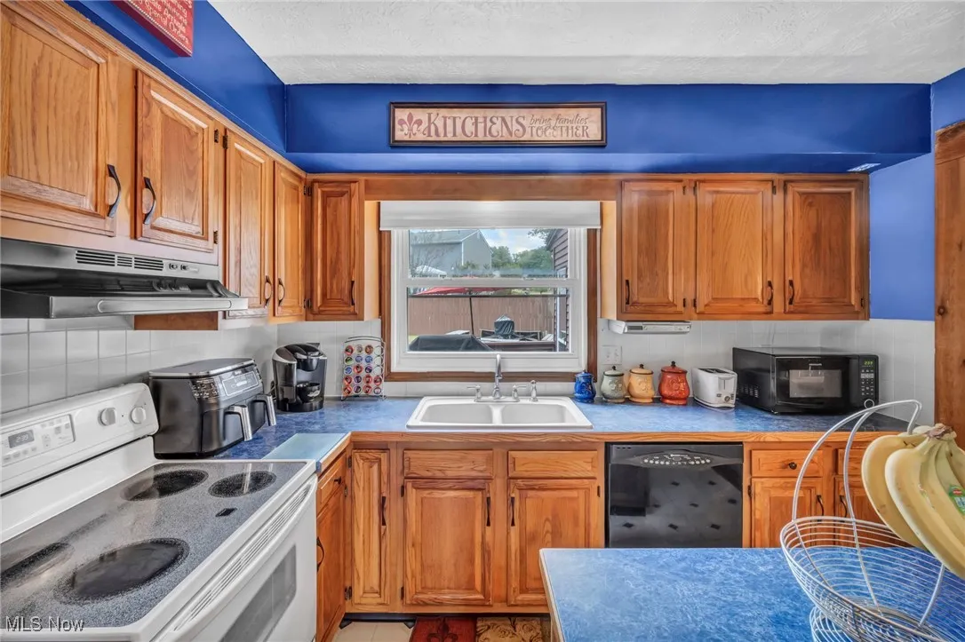 Kitchen with black appliances, decorative backsplash, brown cabinetry, under cabinet range hood, and a textured ceiling