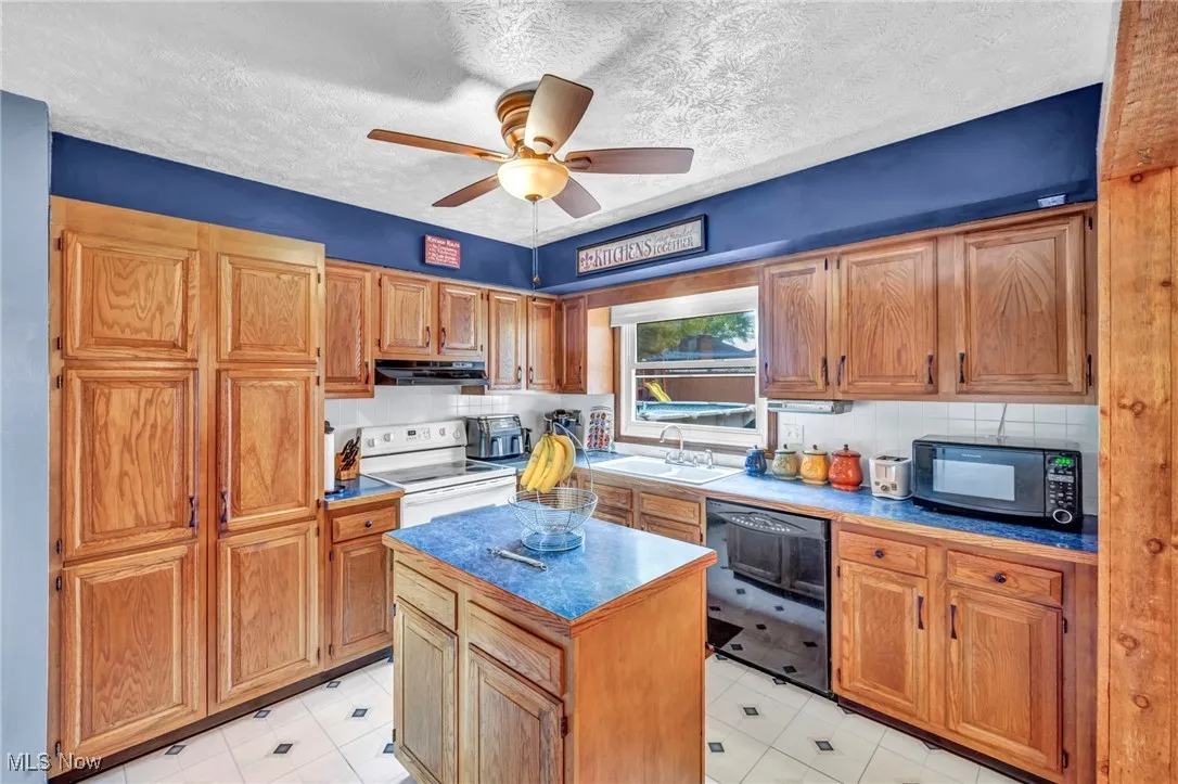 Kitchen with a textured ceiling, black appliances, a center island, a ceiling fan, and brown cabinets