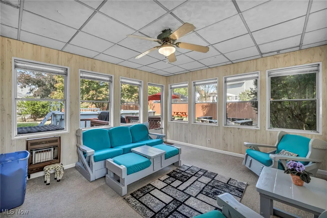 Sunroom with carpet floors, wood walls, heating unit, and a drop ceiling