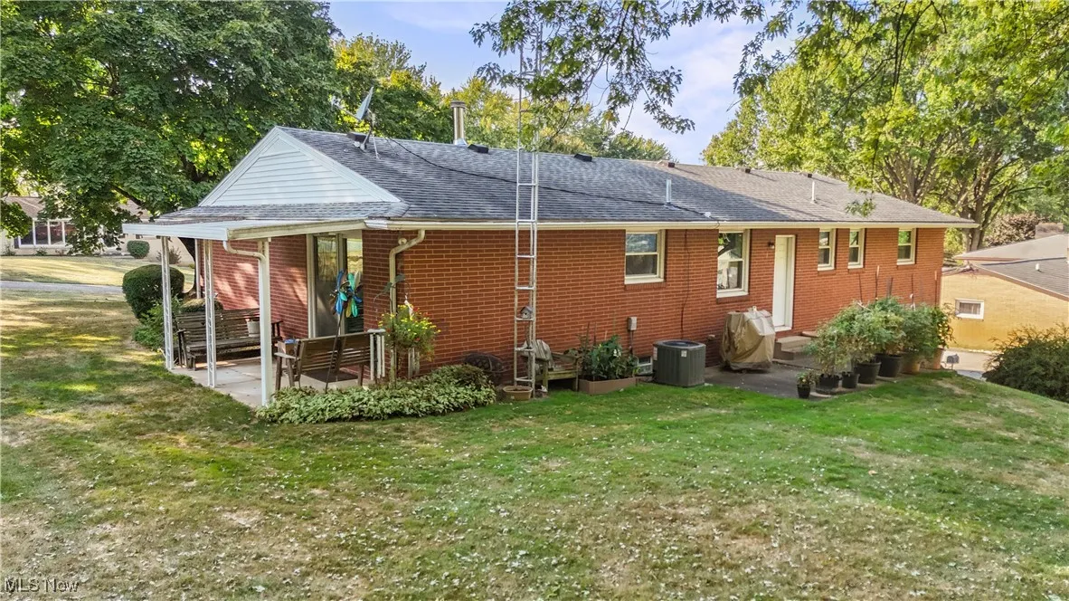 Back of property featuring a lawn, roof with shingles, and brick siding