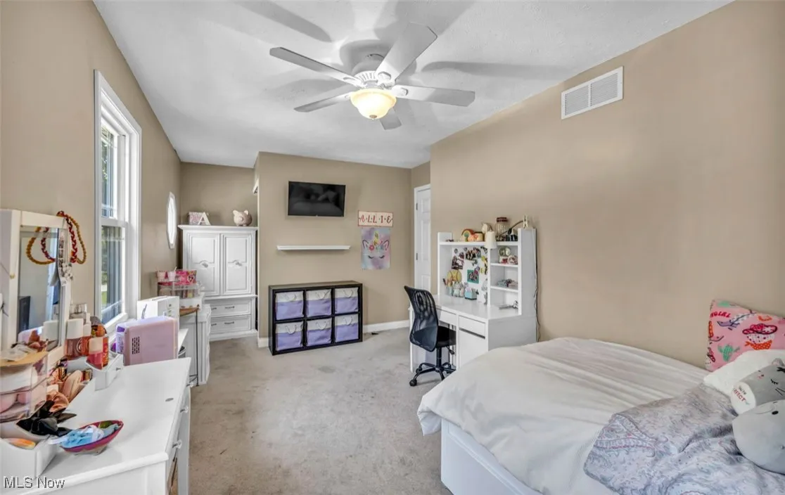 Bedroom featuring light colored carpet, an office area, and a ceiling fan