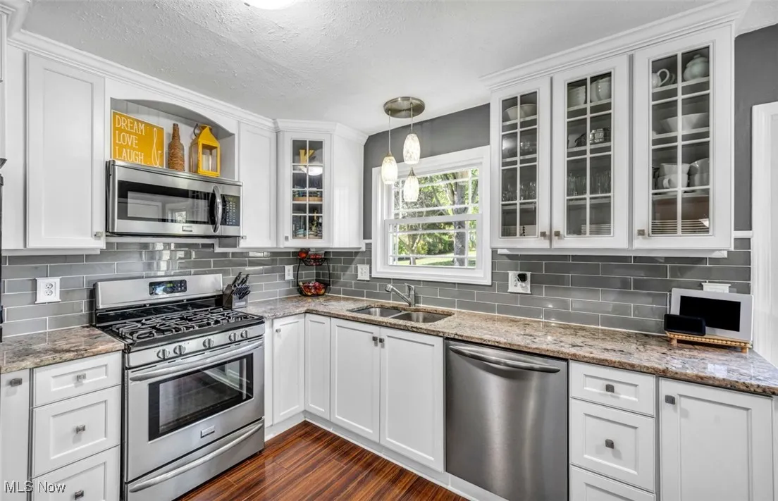Kitchen with appliances with stainless steel finishes, white cabinetry, decorative backsplash, hanging light fixtures, and a textured ceiling