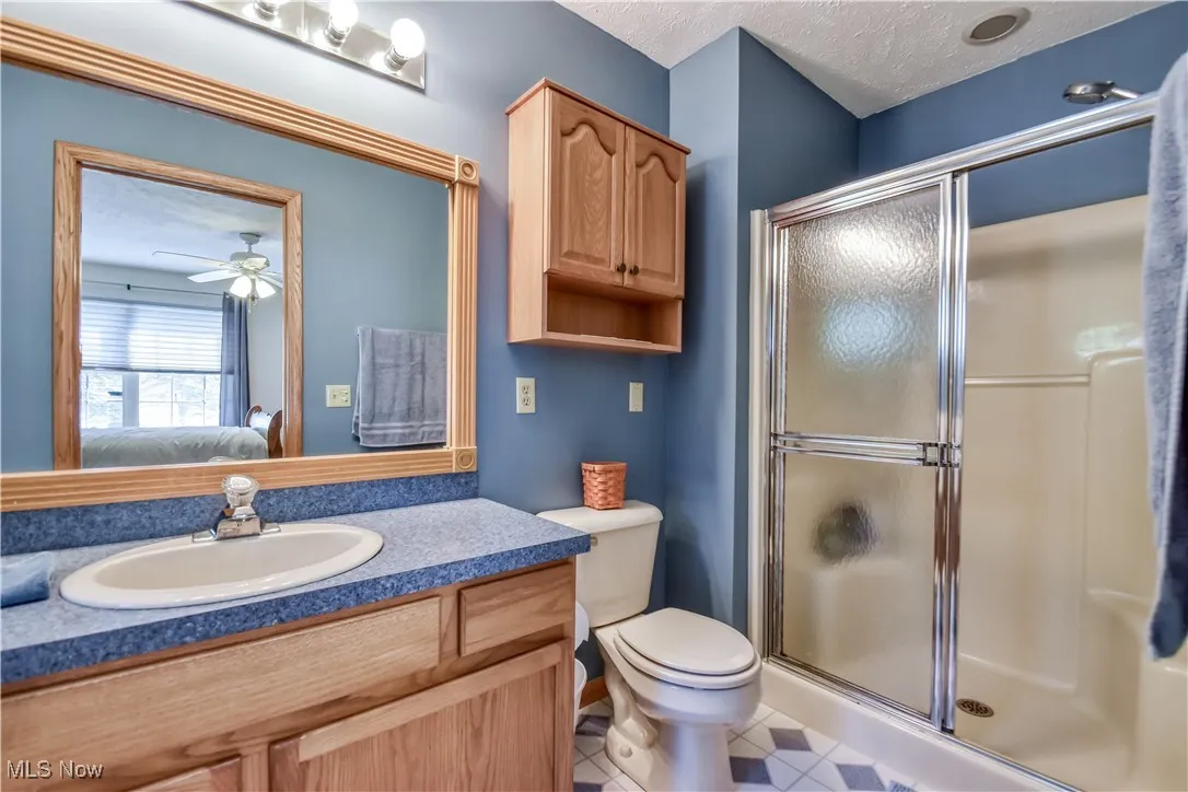 Ensuite bathroom with a stall shower, vanity, a textured ceiling, light tile patterned flooring, and ceiling fan