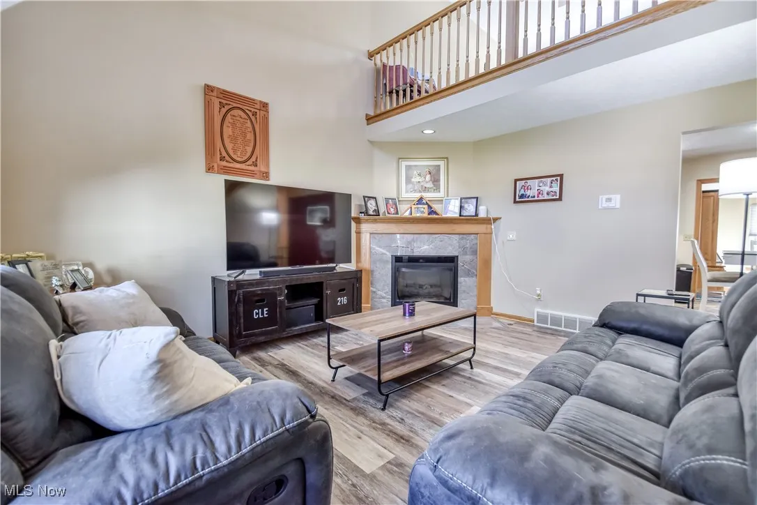 Living room with wood finished floors, a tiled fireplace, and a towering ceiling