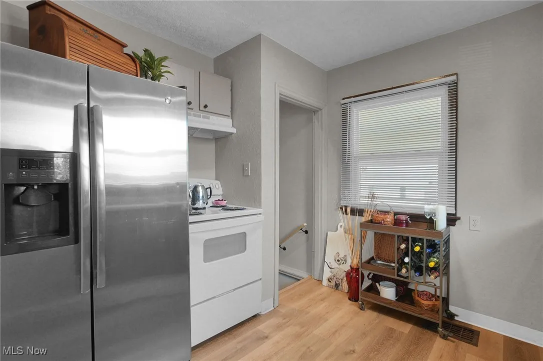 Kitchen featuring stainless steel fridge, white electric range, light wood finished floors, under cabinet range hood, and light countertops