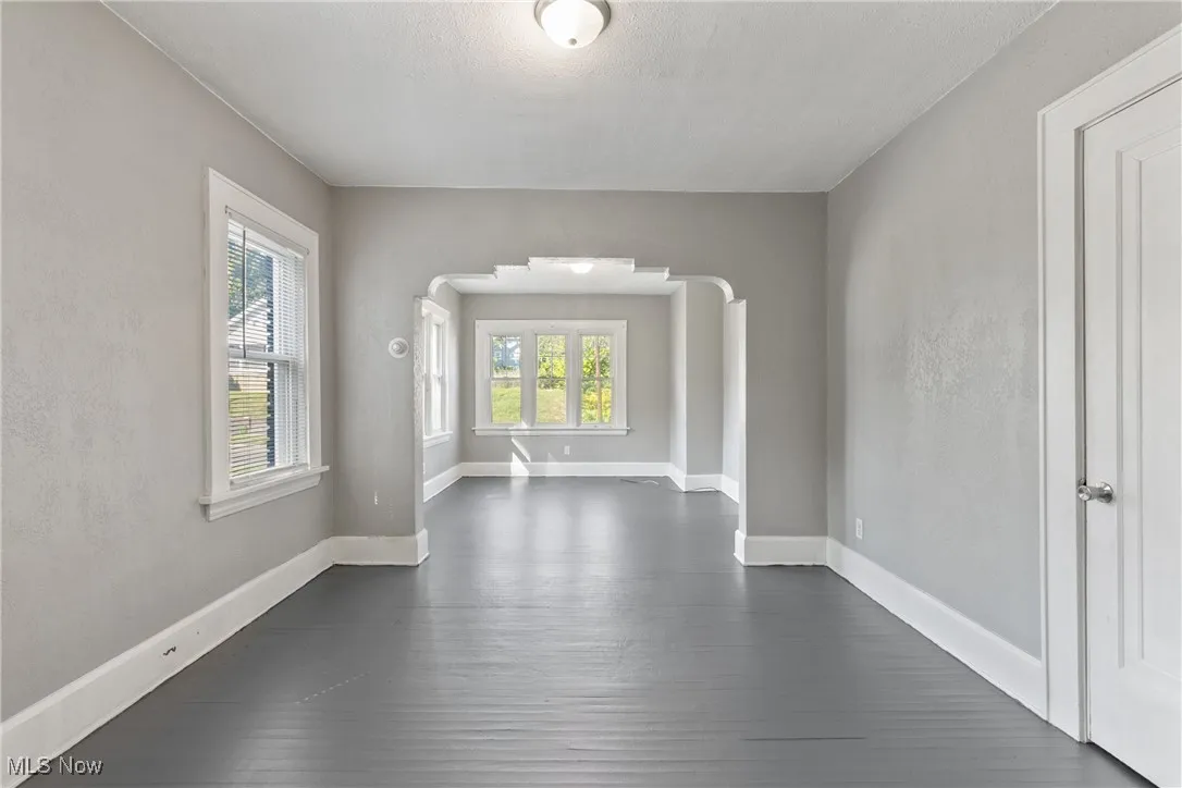 Spare room featuring arched walkways, dark wood finished floors, and a textured wall