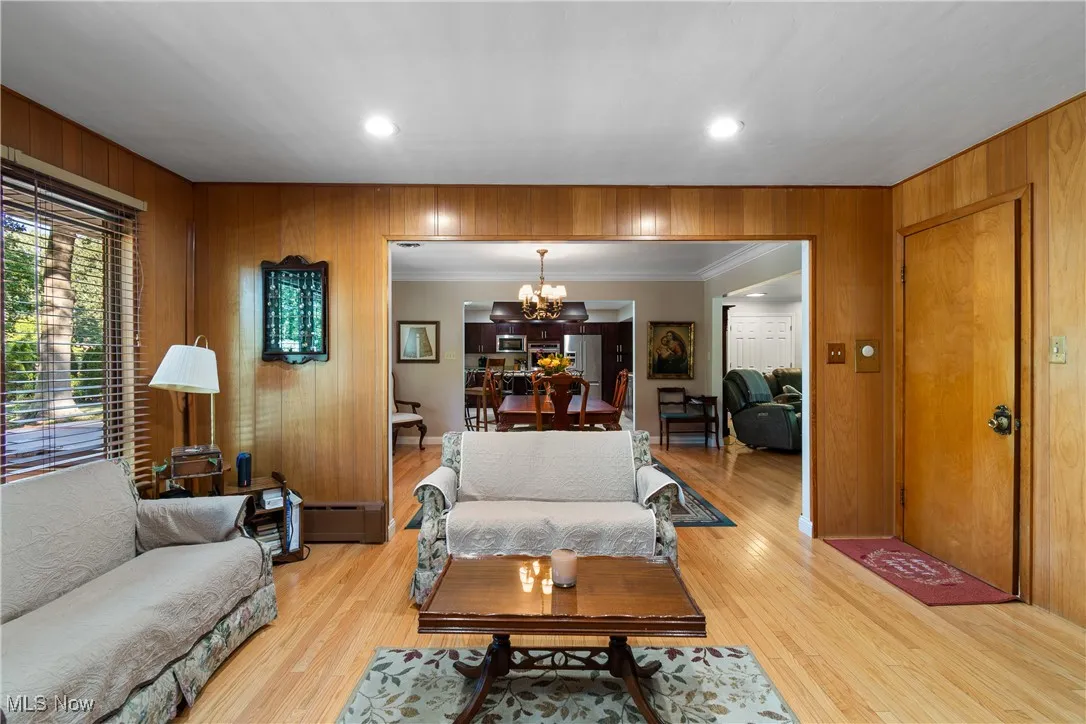 Living room with wood walls, a chandelier, wood finished floors, recessed lighting, and crown molding