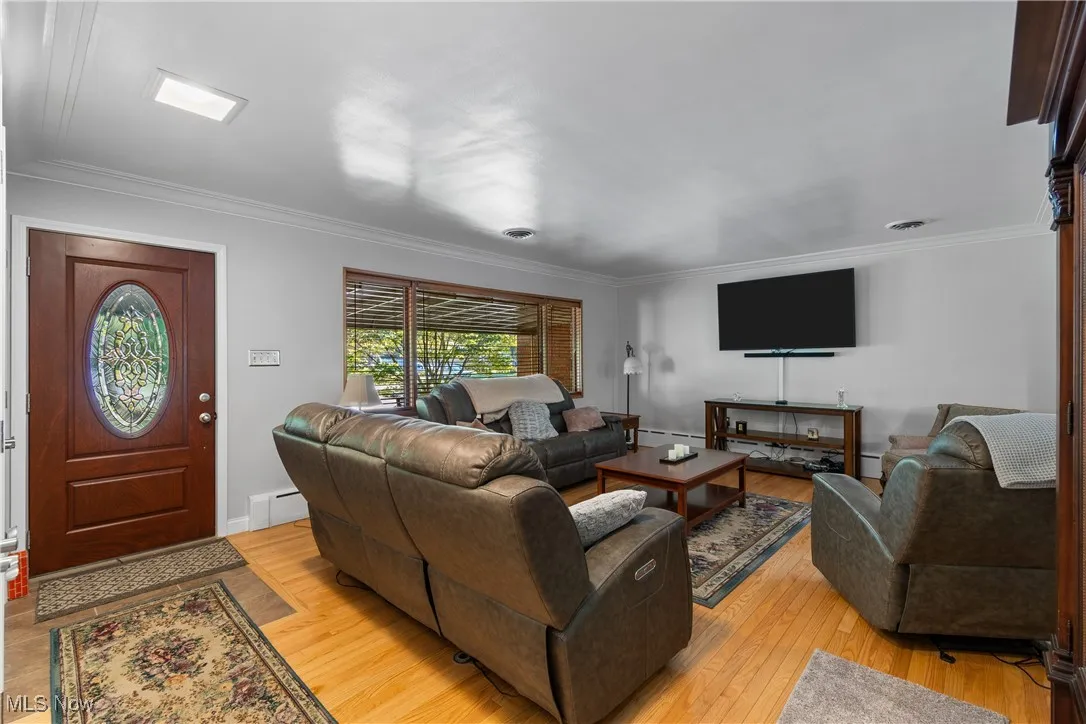 Living area with crown molding, light wood finished floors, and a baseboard heating unit