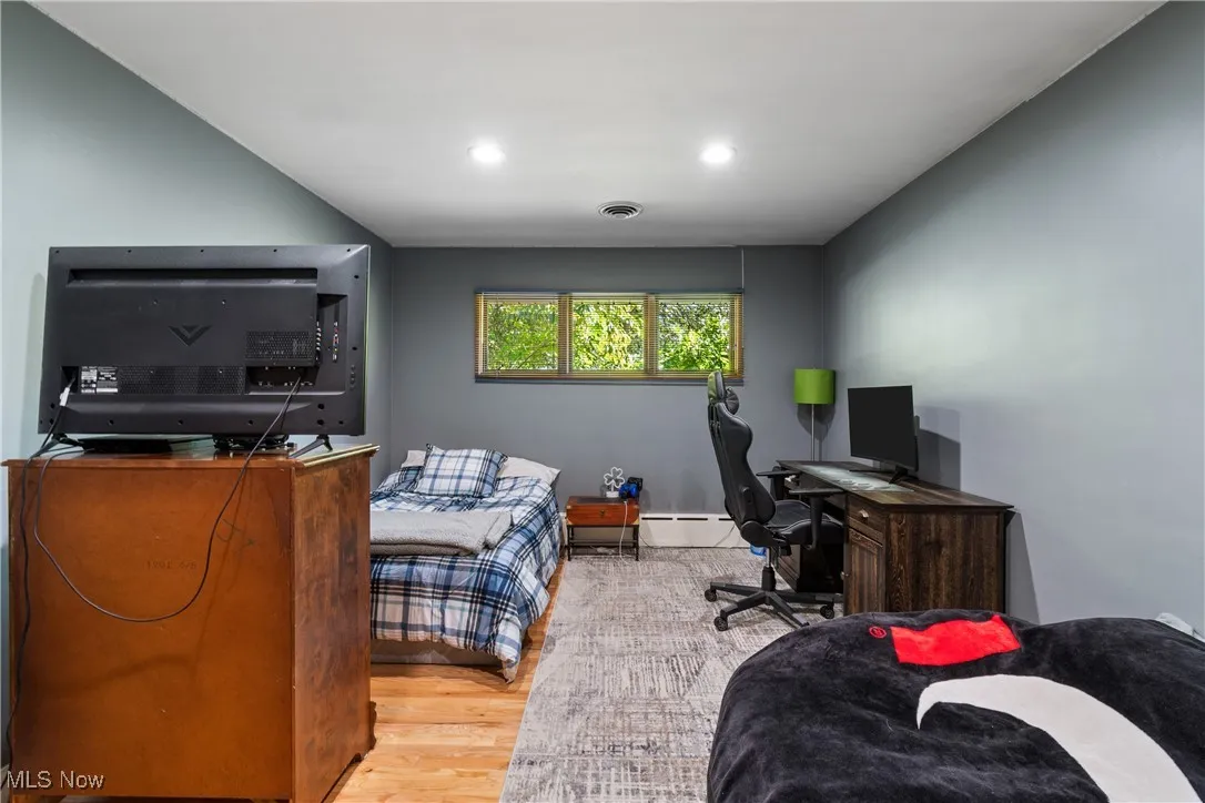 Bedroom featuring wood finished floors, an office area, a baseboard radiator, and recessed lighting
