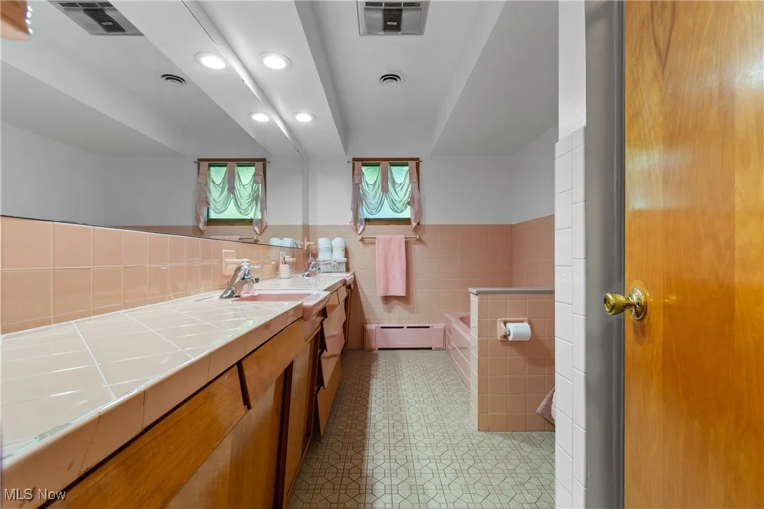 Full bathroom with double vanity, a bath, baseboard heating, recessed lighting, and tile walls