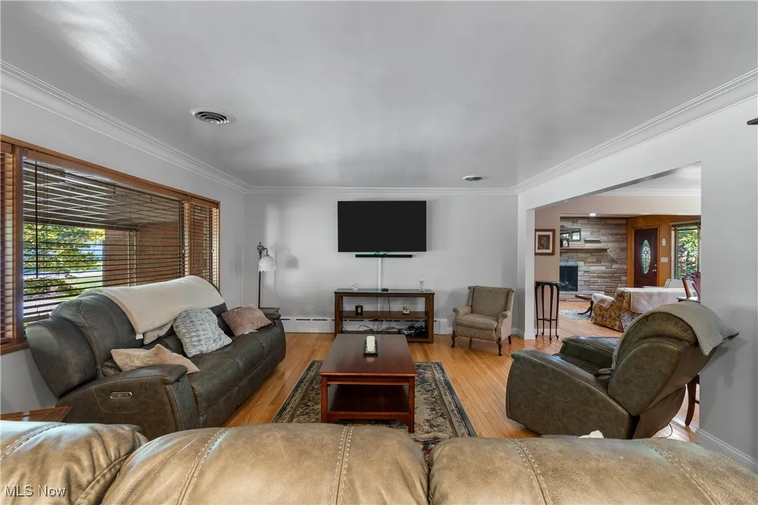 Living room with ornamental molding, wood finished floors, and a stone fireplace