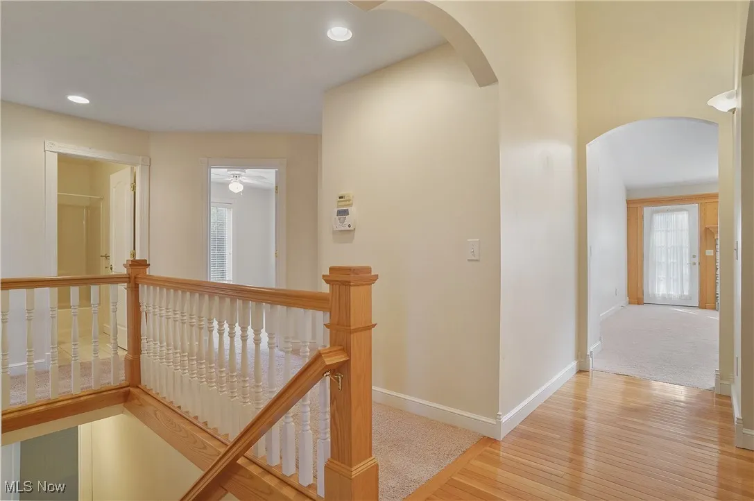 Hall with an upstairs landing, light wood finished floors, arched walkways, recessed lighting, and light colored carpet