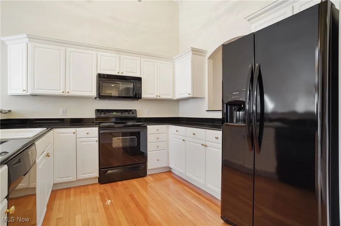Kitchen with black appliances, black granite, white cabinets, and light wood finished floors