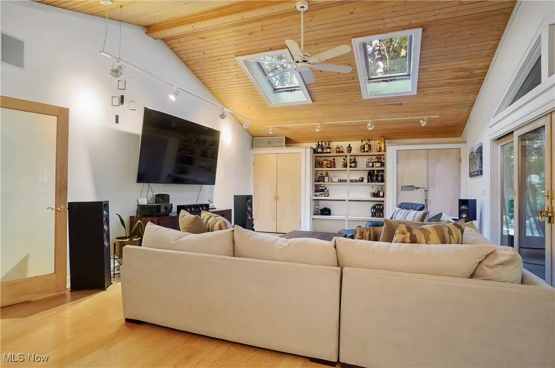 Living area with wood ceiling, a skylight, a ceiling fan, light wood-style flooring, and high vaulted ceiling