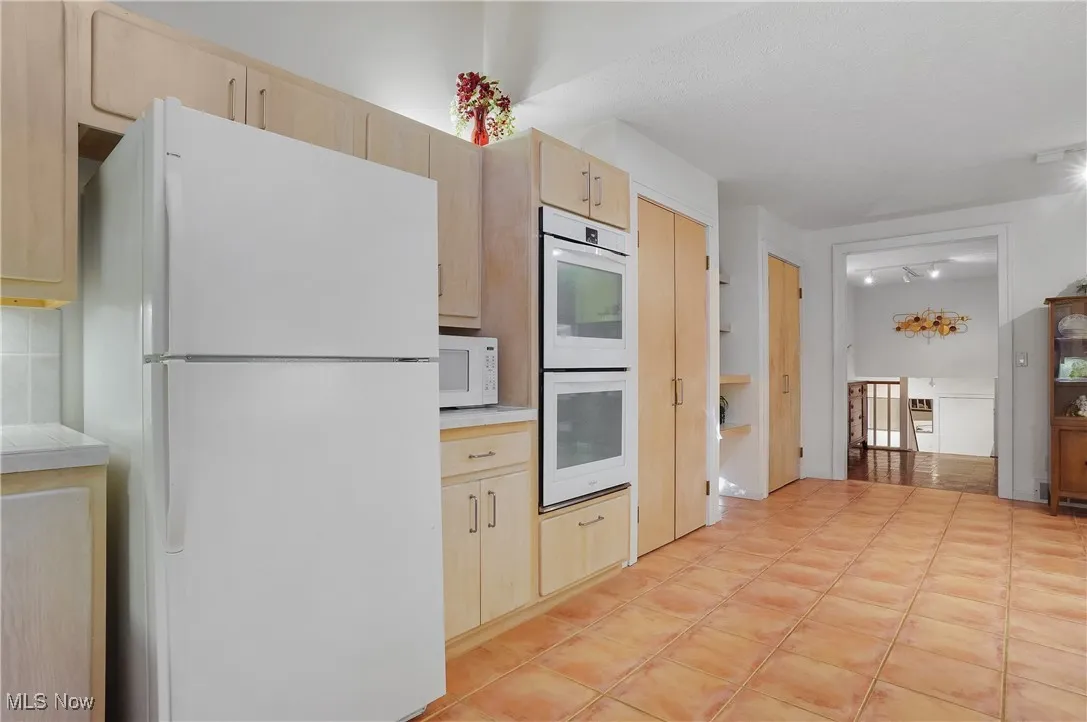 Kitchen featuring white appliances, light brown cabinets, and light tile patterned floors