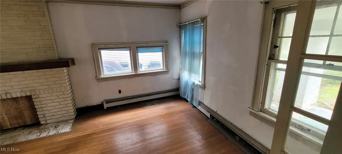 Unfurnished living room with wood-type flooring, baseboard heating, and a brick fireplace