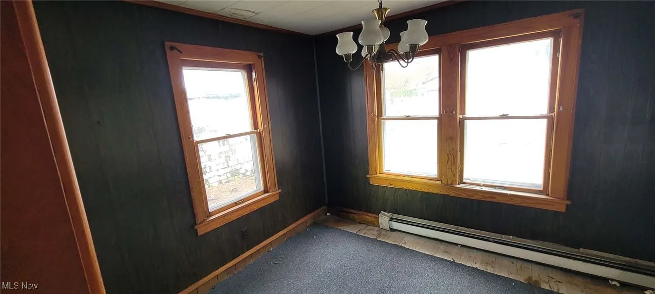Empty room featuring a chandelier, a baseboard heating unit, and wood walls