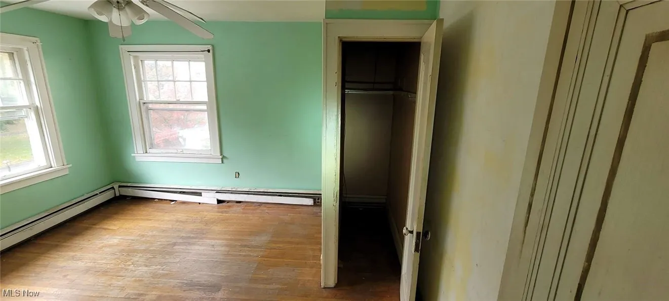 Unfurnished bedroom with hardwood / wood-style floors, a ceiling fan, and a baseboard heating unit