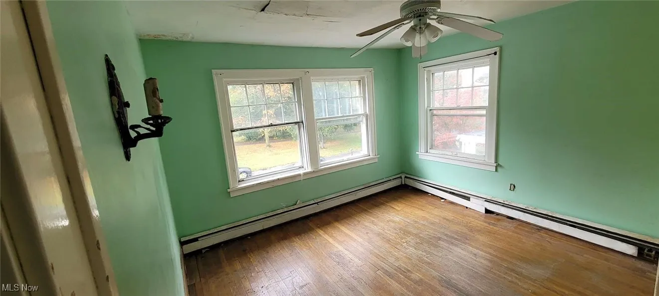 Unfurnished room featuring baseboard heating, hardwood / wood-style floors, and ceiling fan