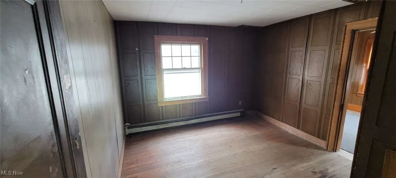 Empty room with wood-type flooring, wood walls, and a baseboard radiator