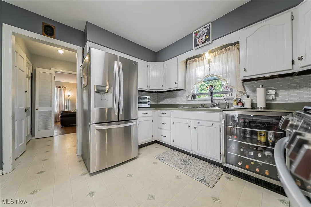 Kitchen with appliances with stainless steel finishes, white cabinetry, tasteful backsplash, and wine cooler