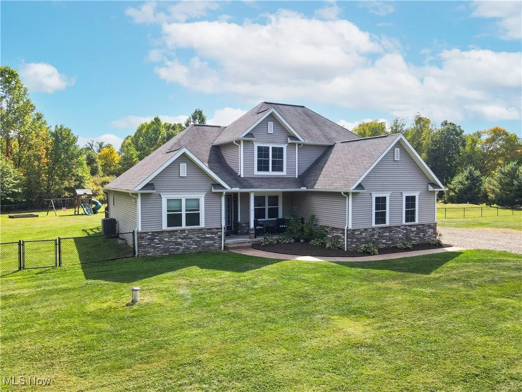 View of front of house with stone siding, a porch, a playground, a shingled roof, and a gate