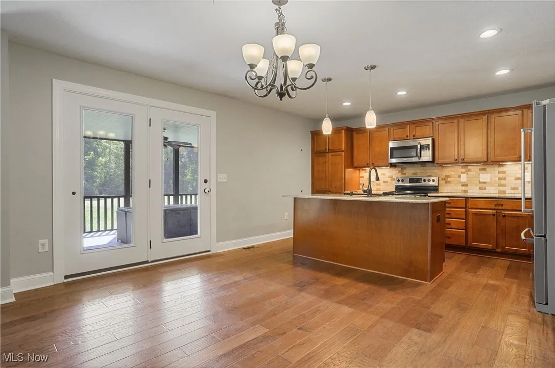 Kitchen featuring decorative backsplash, recessed lighting, brown cabinets, a chandelier, and a kitchen island with sink
