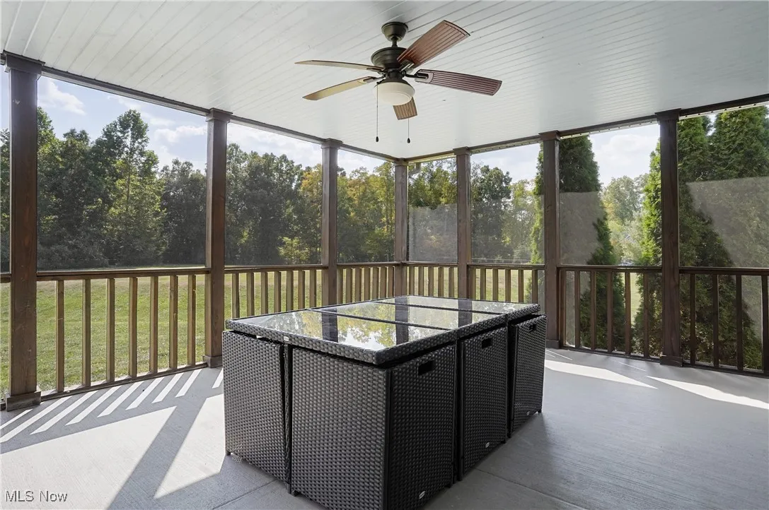 Sunroom featuring plenty of natural light, view of wooded area, and ceiling fan