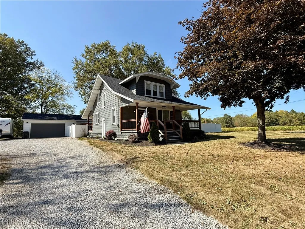 View of front facade with an outbuilding, a porch, a garage, gravel driveway, and a front yard