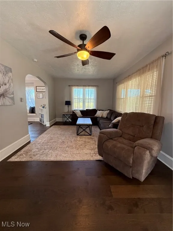 Living area featuring a textured ceiling, arched walkways, healthy amount of natural light, dark wood-style flooring, and a ceiling fan
