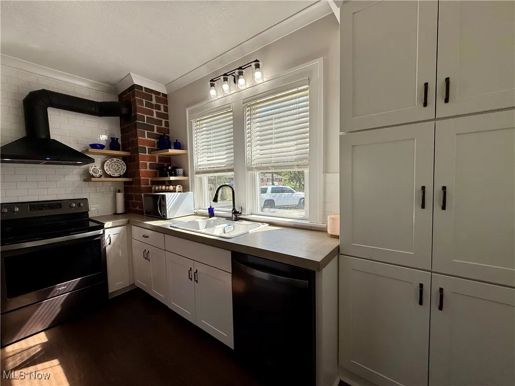 Kitchen featuring stainless steel range with electric cooktop, wall chimney range hood, white cabinets, dishwasher, and tasteful backsplash