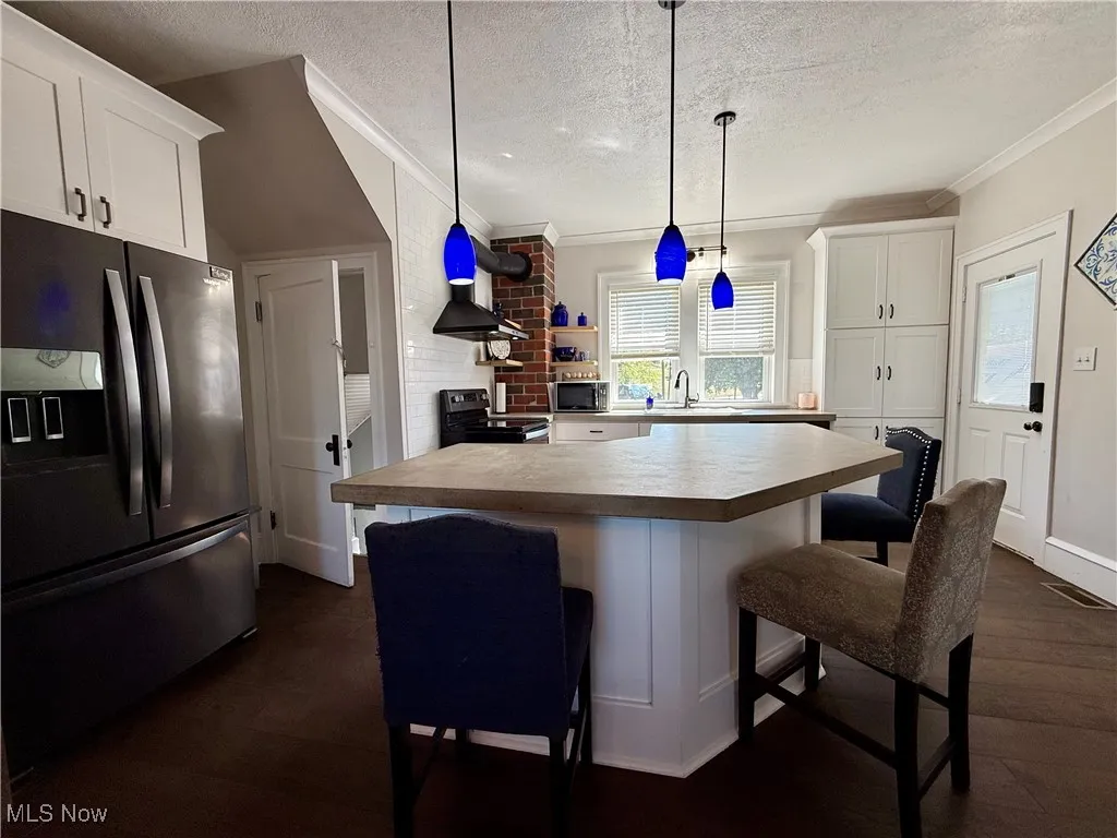 Kitchen featuring white cabinetry, stainless steel appliances, a kitchen breakfast bar, light countertops, and decorative light fixtures