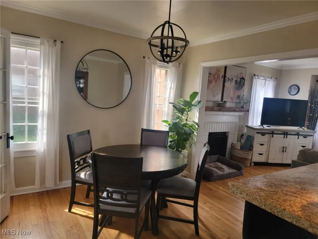Dining room featuring a brick fireplace, crown molding, light wood-type flooring, and a chandelier