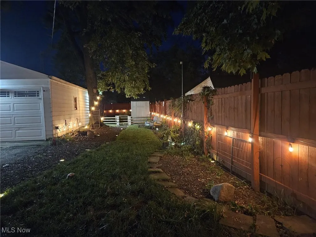 Yard at night with a fenced backyard, an outdoor structure, and a garage