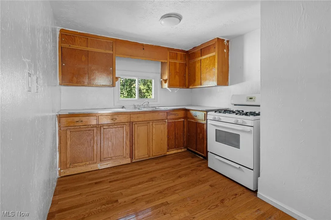 Kitchen with a textured wall, white gas range oven, light countertops, light wood-type flooring, and a textured ceiling