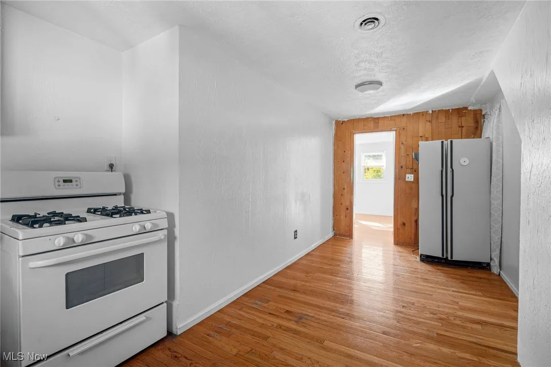 Kitchen featuring white appliances, light wood-style flooring, a textured ceiling, and wooden walls
