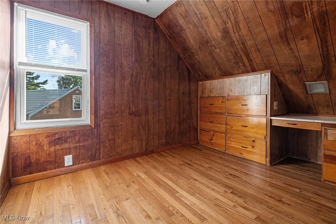 Additional living space with wooden walls, lofted ceiling, and light wood-style flooring
