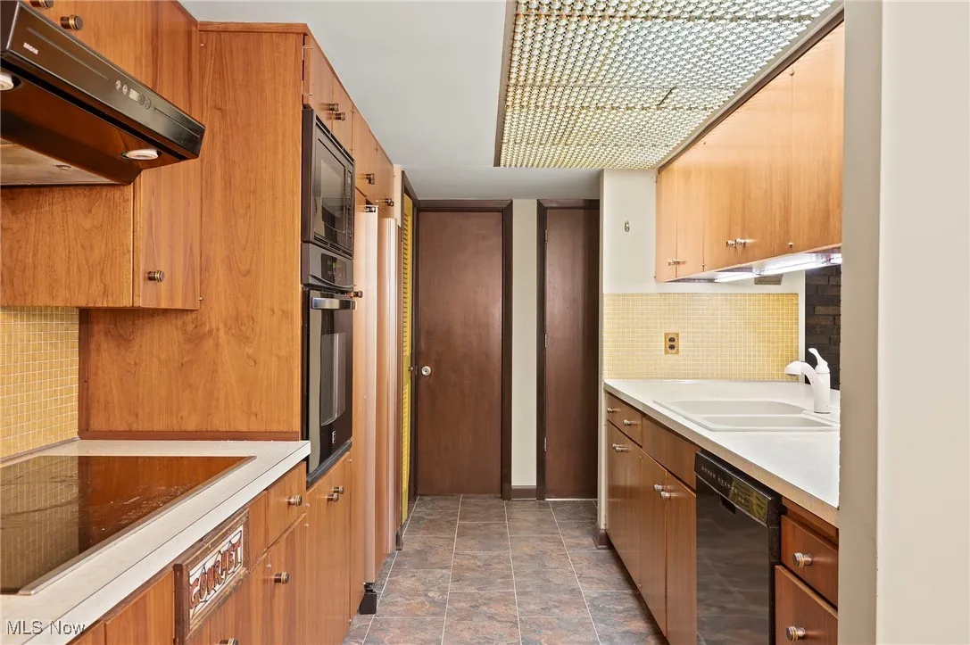 Kitchen with tasteful backsplash, light countertops, range hood, and black appliances