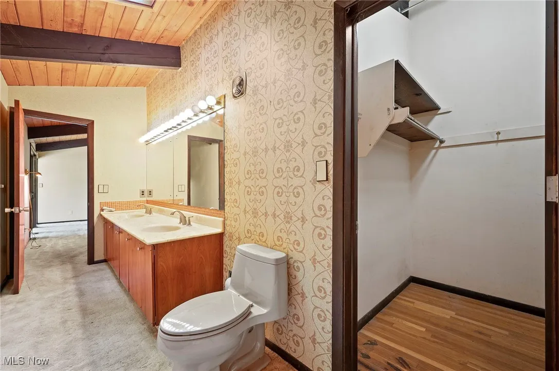 Bathroom with wallpapered walls, double vanity, wood ceiling, and light wood-style flooring
