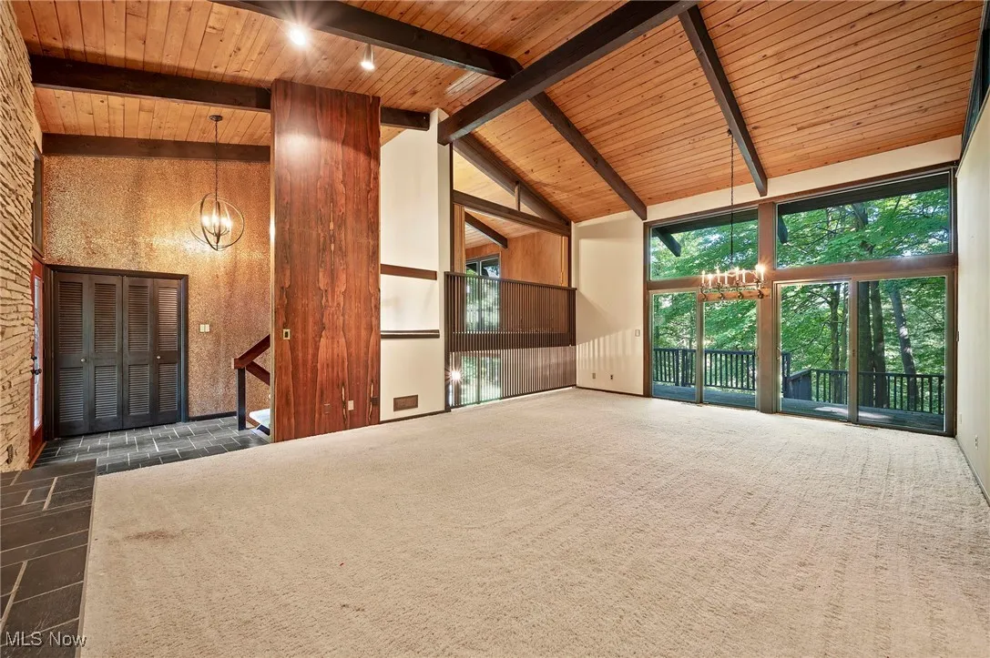 Unfurnished living room featuring a chandelier, a wood ceiling with exposed beams, high vaulted ceiling, and dark carpet