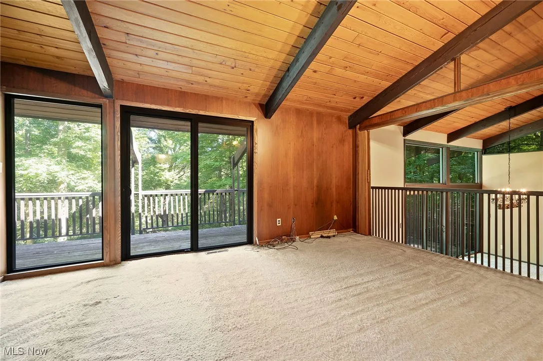 Empty room featuring carpet floors, wooden ceiling, wood walls, and a chandelier
