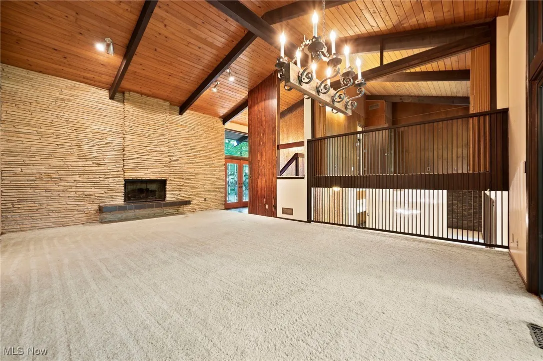 Unfurnished living room with carpet flooring, high vaulted ceiling, a wood ceiling with exposed beams, a chandelier, and a fireplace