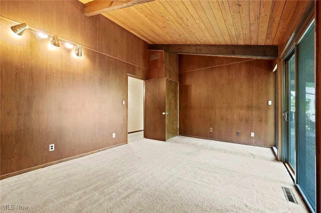 Empty room with beamed ceiling, wood walls, light carpet, and high vaulted ceiling